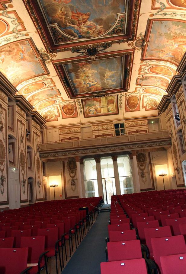 Ein prunkvoller Konzertsaal mit rotem Gestühl und Deckenmalereien.