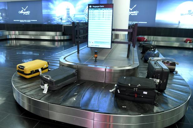 Ein Gepäckband am Flughafen mit mehreren Koffern und einem Bildschirm mit Ankunftszeiten.