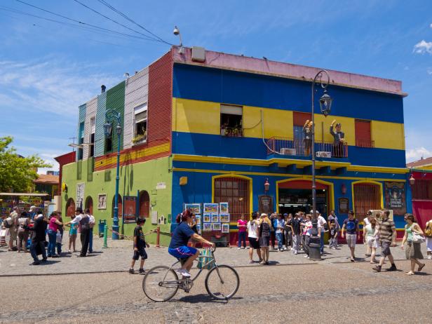 Buntes Gebäude in La Boca, Buenos Aires, mit Menschen und einer Radfahrerin im Vordergrund.