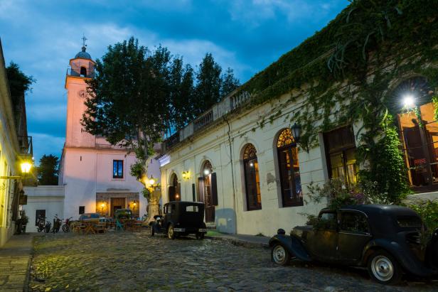 Kopfsteinpflasterstraße mit Oldtimern und einem Kirchturm in Colonia del Sacramento, Uruguay.
