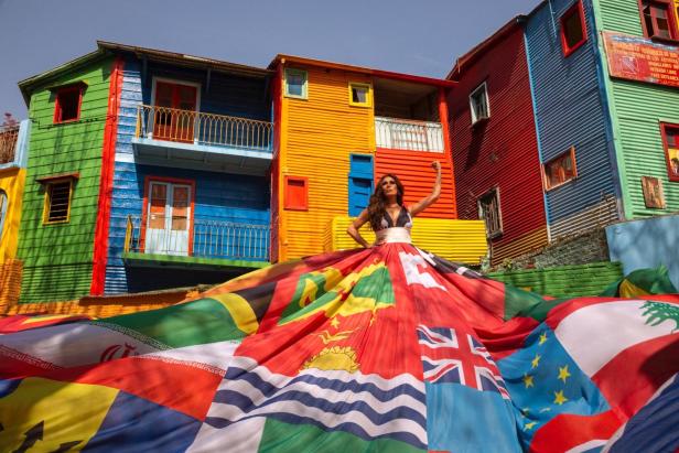 Eine Frau in einem Kleid aus Flaggen vor bunten Häusern in La Boca, Buenos Aires.