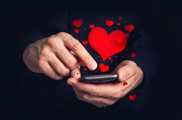 Ein Mann tippt auf ein Smartphone, umgeben von roten Herzen.
