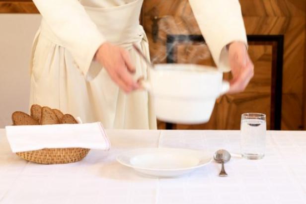 Eine Person in weißer Kleidung serviert dampfende Suppe an einem gedeckten Tisch.