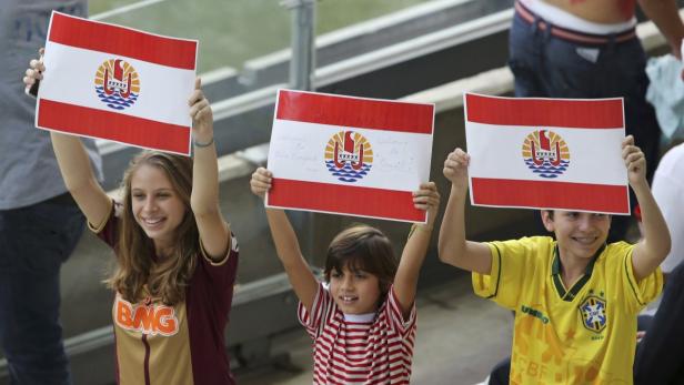 Drei Kinder halten Schilder mit der Flagge von Tahiti hoch.