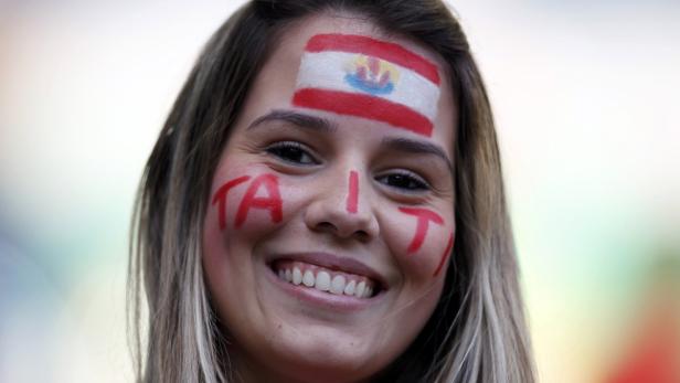 Eine lächelnde Frau mit der Aufschrift „TAITI“ und der Flagge von Tahiti auf dem Gesicht.