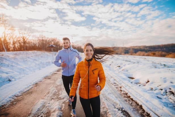 Ein Paar joggt im Winter auf einer schneebedeckten Straße.