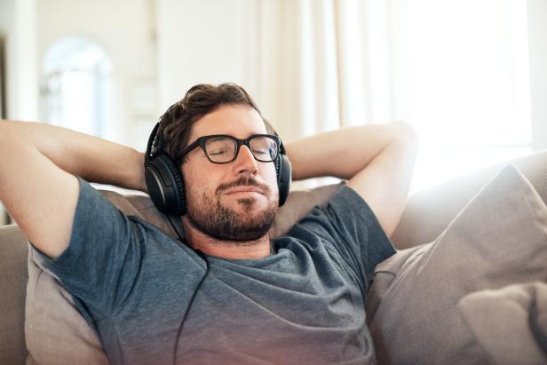 Ein Mann mit Brille und Kopfhörern entspannt sich auf einem Sofa.