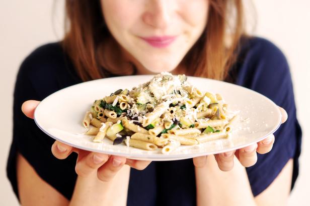 Eine Frau präsentiert einen Teller Penne mit Gemüse und Käse.