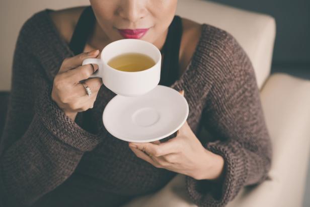 Eine Frau mit rotem Lippenstift trinkt Tee aus einer weißen Tasse.