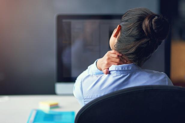 Eine Frau massiert ihren Nacken vor einem Computer.