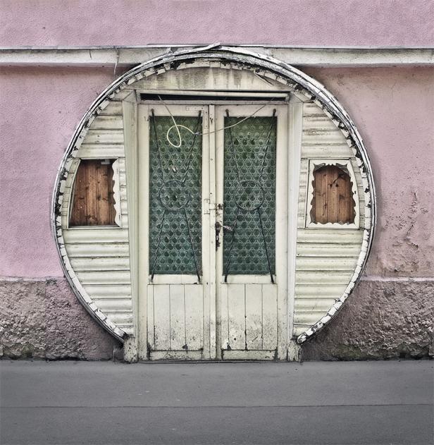 Eine ungewöhnliche, runde Tür mit kleinen Fenstern in einer rosa Wand.