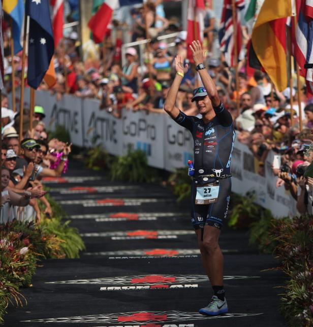 Ein Triathlet überquert die Ziellinie eines Ironman-Rennens und jubelt.