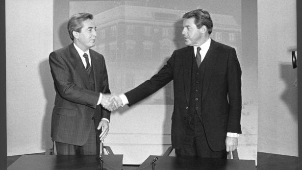 Zwei Männer in Anzügen geben sich die Hand vor einem Gebäude.