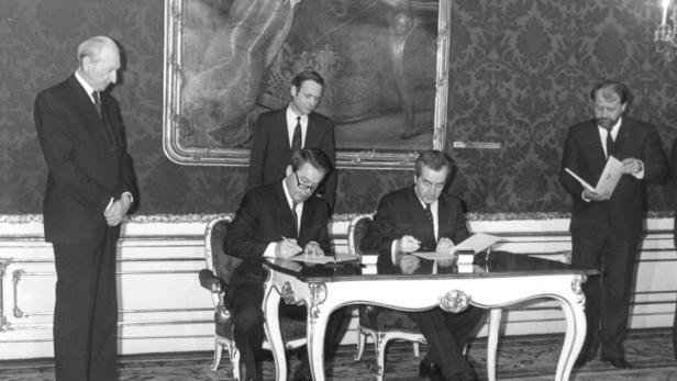 Zwei Männer unterzeichnen ein Dokument an einem verzierten Tisch.