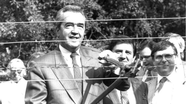 Ein Mann im Anzug durchtrennt mit einer Zange einen Stacheldrahtzaun.