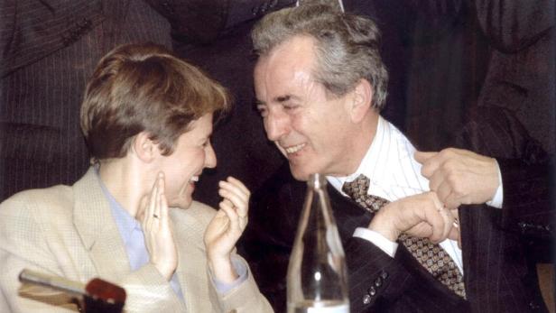 Eine lachende Frau und ein Mann im Anzug unterhalten sich angeregt.