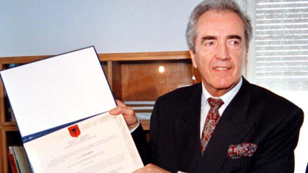 Ein Mann im Anzug hält eine Urkunde mit dem albanischen Wappen in der Hand.