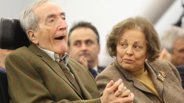 Ein älterer Mann im Rollstuhl und eine ältere Frau sitzen nebeneinander bei einer Veranstaltung.