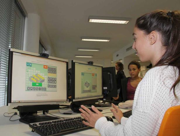 Eine junge Frau arbeitet an zwei Computern mit einer Programmieroberfläche.