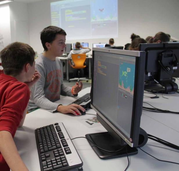 Zwei Jungen arbeiten an Computern in einem Klassenzimmer und lernen Programmieren.