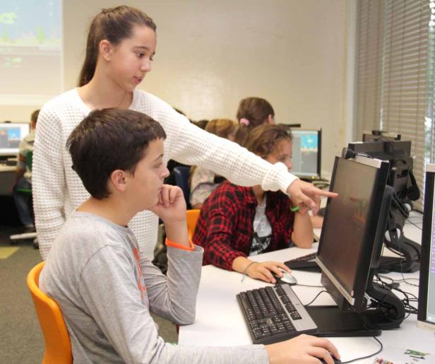 Schüler arbeiten im Computerraum, ein Mädchen zeigt auf den Bildschirm eines anderen Schülers.