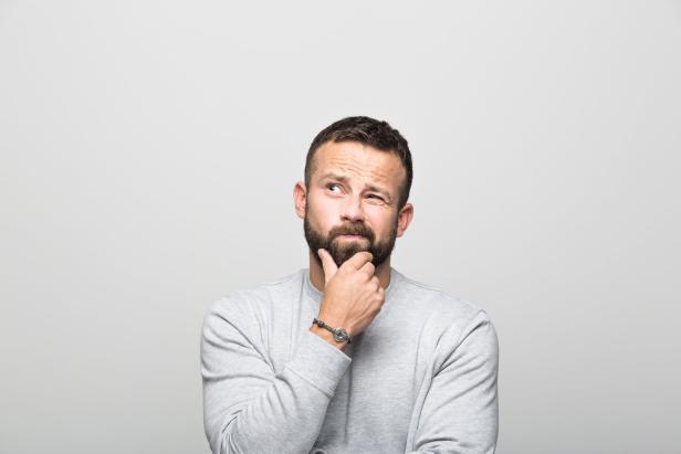 Ein bärtiger Mann mit grauem Pullover wirkt nachdenklich.
