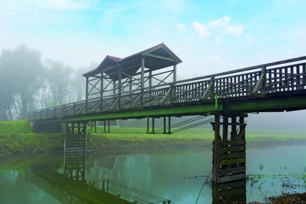 Eine hölzerne Fußgängerbrücke mit Überdachung überspannt einen Fluss im Nebel.