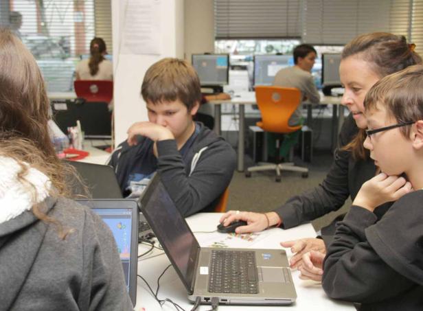 Schüler arbeiten mit einer Lehrerin an Laptops in einem Klassenzimmer.
