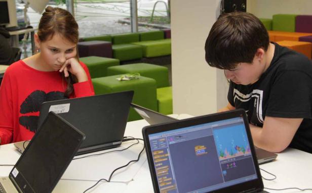 Zwei Jugendliche arbeiten an Laptops mit Programmier-Software.