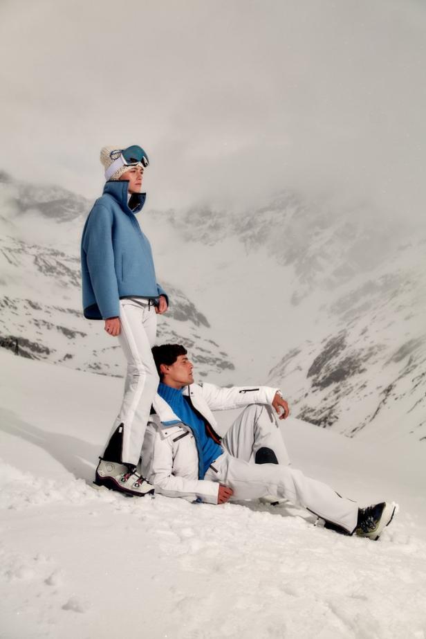 Ein Mann und eine Frau in Skibekleidung posieren vor einer verschneiten Bergkulisse.