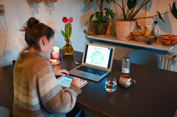 Eine Frau arbeitet an einem Tisch mit Laptop und Tablet, umgeben von Blumen und Getränken.