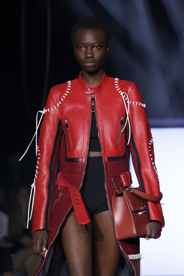 Eine Frau mit roter Lederjacke und passender Handtasche auf dem Laufsteg.