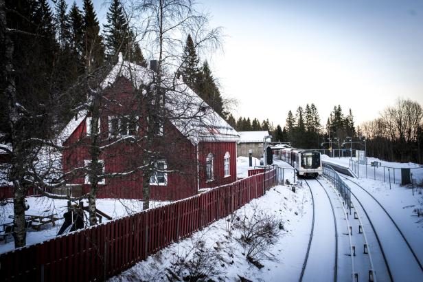 Ein rotes Holzhaus steht neben einer schneebedeckten Bahnhaltestelle.