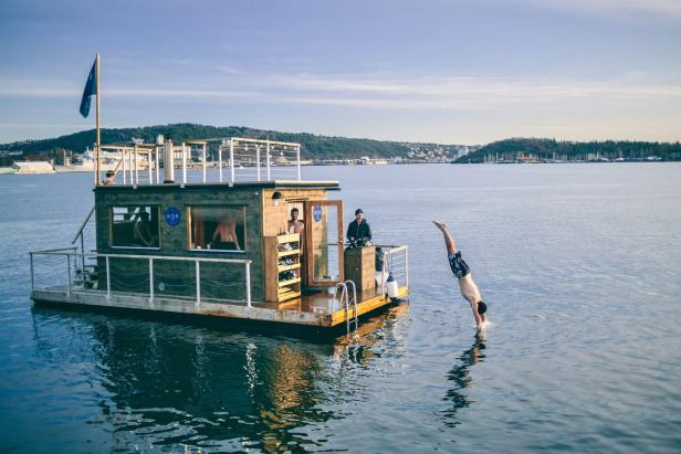 Ein Mann springt von einer schwimmenden Sauna ins Wasser.