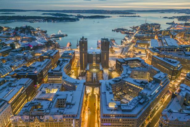 Luftaufnahme von Oslo im Winter mit dem beleuchteten Rathaus im Zentrum.