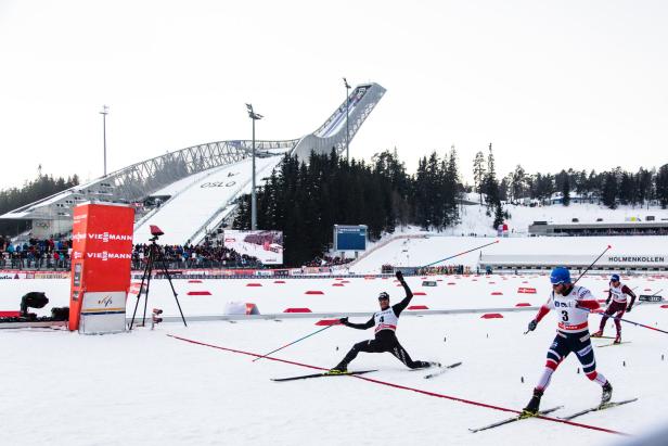 Ein Skilangläufer stürzt im Schnee, während andere Läufer in Holmenkollen vorbeiziehen.