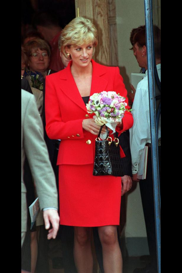 Diana, Prinzessin von Wales, in einem roten Kostüm mit Blumenstrauß und Handtasche.