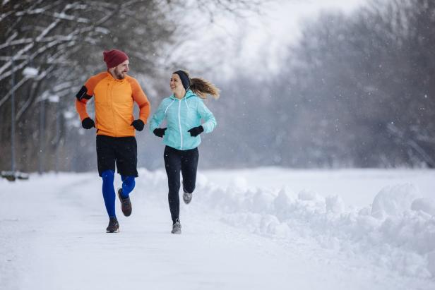 Ein Mann und eine Frau joggen im Winter durch eine verschneite Landschaft.