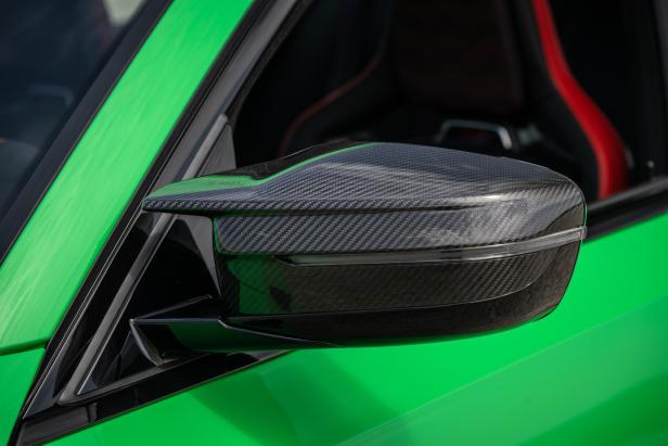 Der Außenspiegel eines grünen BMW M3 mit Carbon-Elementen.