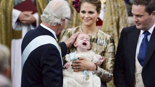 König Carl XVI. Gustaf berührt das weinende Baby, das Prinzessin Madeleine hält.