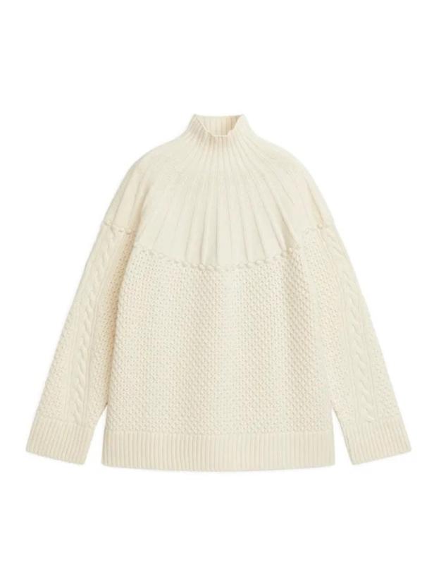 Ein cremefarbener Strickpullover mit Rollkragen und verschiedenen Strickmustern.