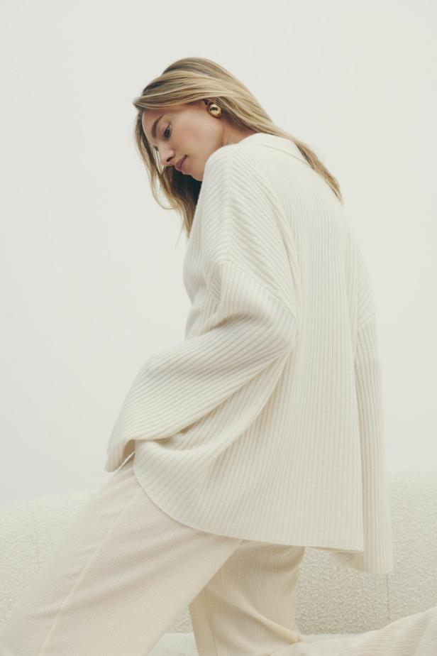 Eine blonde Frau trägt einen cremefarbenen Strickpullover und passende Hose.