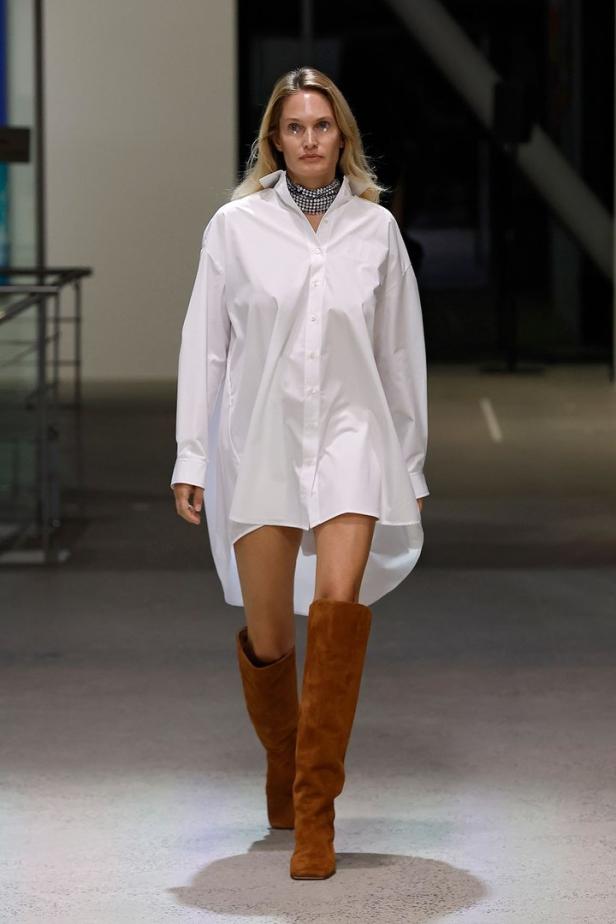 Eine Frau mit blonden Haaren trägt ein weißes Hemd und braune Stiefel.