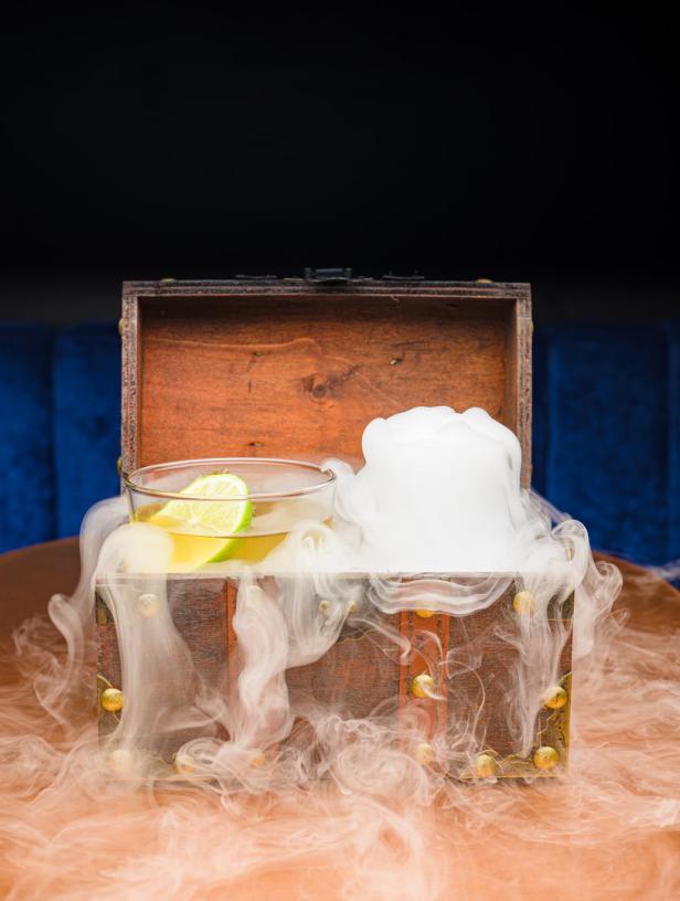 Ein Cocktail mit Limette steht in einer Holztruhe, umgeben von Trockeneisnebel.