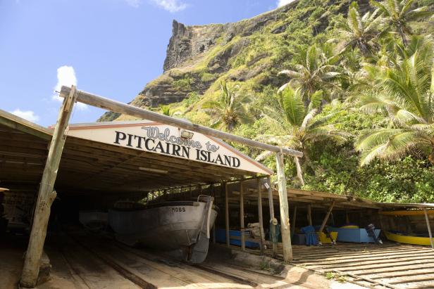 Ein Bootsanleger mit dem Schild „Welcome to Pitcairn Island“ vor einer grünen Hügellandschaft.