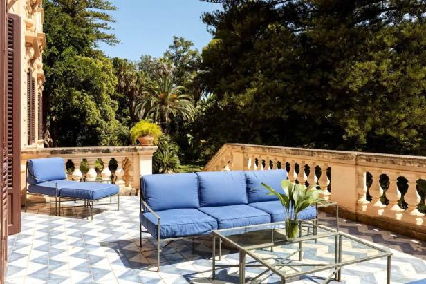 Eine blaue Couch und ein Sessel stehen auf einer Terrasse mit Blick auf einen üppigen Garten.
