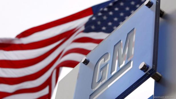 Das GM-Logo vor einer wehenden US-amerikanischen Flagge.