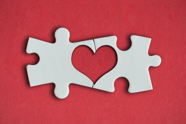 Zwei Puzzleteile bilden zusammen eine Herzform auf rotem Hintergrund.