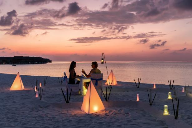 Ein Paar genießt ein romantisches Abendessen am Strand bei Sonnenuntergang, beleuchtet von Laternen.
