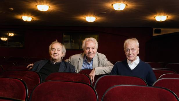 Drei ältere Männer sitzen in einem leeren Theatersaal.